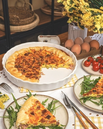 Maradékmentő sonkás pite fehér sütőtálban, friss rukkolával tálalva asztalon